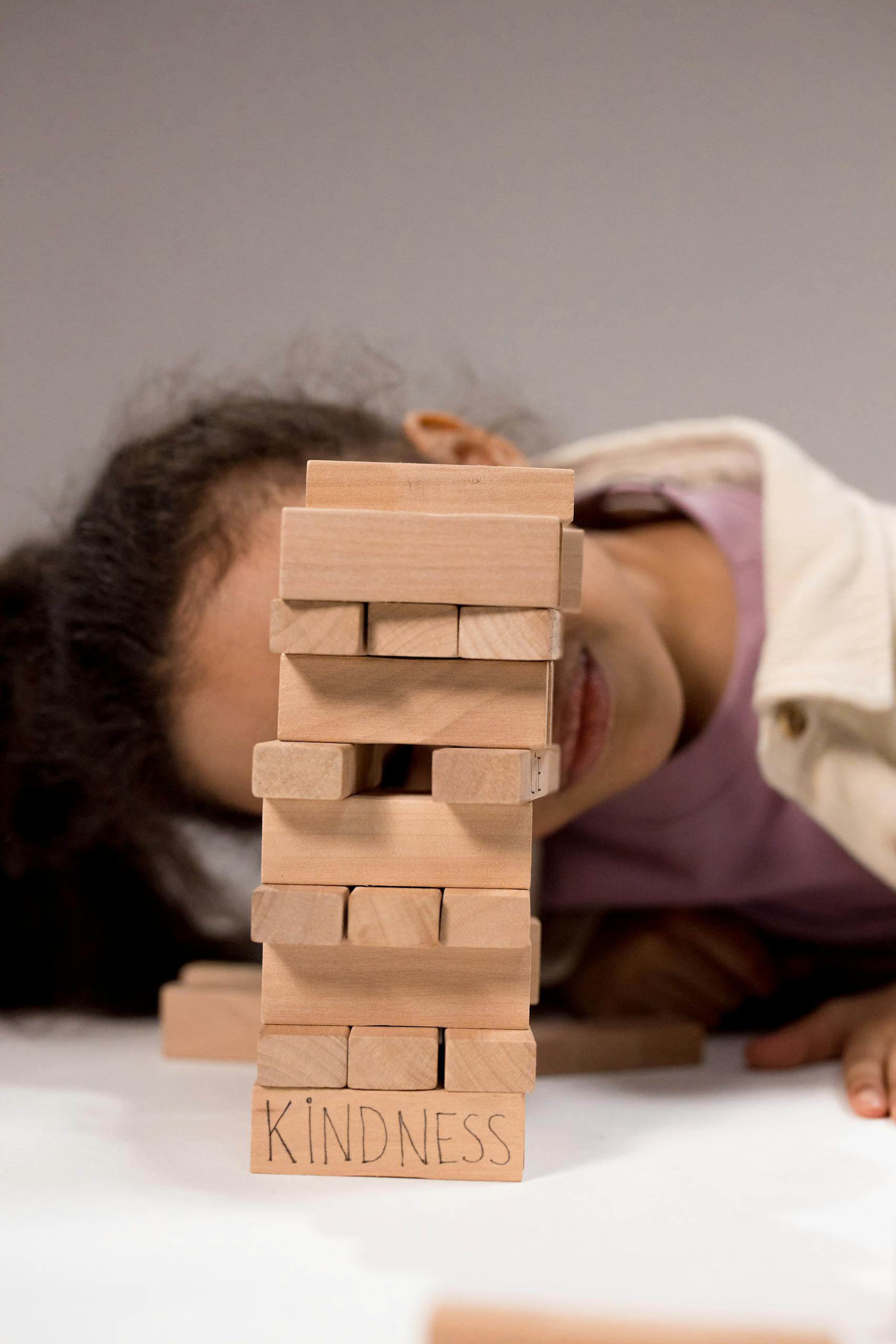 Girl playing Jenga, focused on kindness message on block. Childhood and playtime concept.